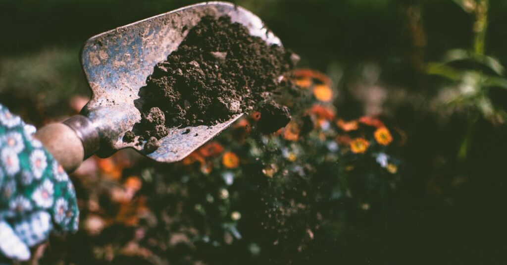 Close-up of a gardening shovel with soil, surrounded by vibrant blooms in an outdoor garden setting.